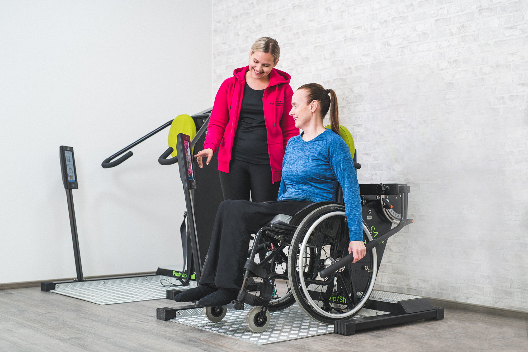 A physiotherapist assists a woman in a wheelchair using accessible strength equipment, illustrating an accessible strength equipment.
