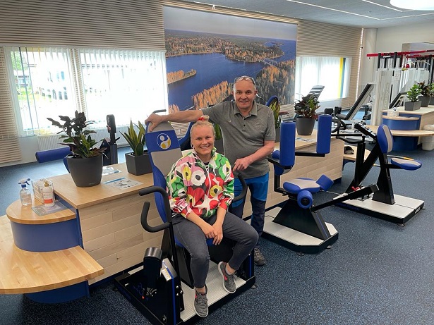 Two people smiling near HUR gym machines.